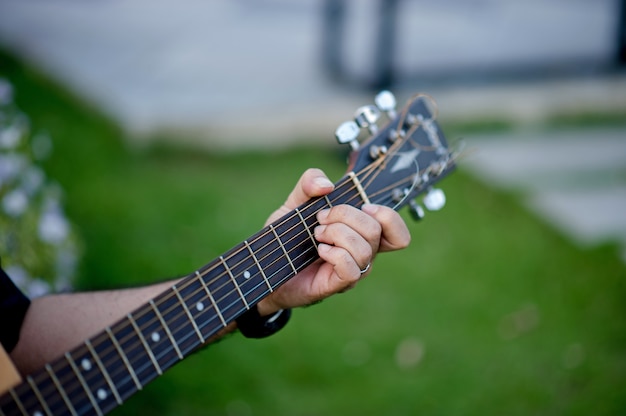 Beeld van een gitarist, een jonge mens die een gitaar speelt terwijl het zitten in een natuurlijke tuin, muziekconcept