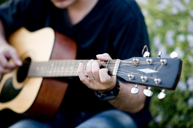 Beeld van een gitarist, een jonge mens die een gitaar speelt terwijl het zitten in een natuurlijke tuin, muziekconcept