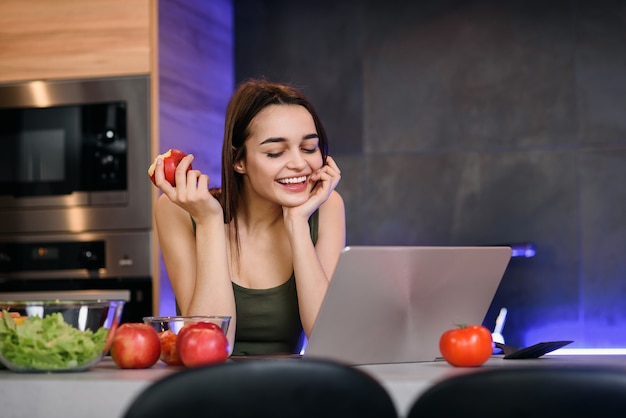 Beeld van een mooi jong studentenmeisje met appelzitting binnen gebruikend laptop computer.