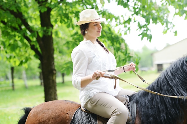 Beeld van gelukkige vrouwelijke zitting op paard bij dorpslandbouwbedrijf