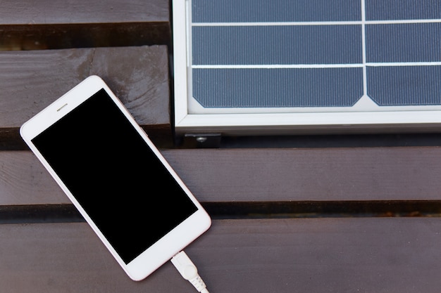 Foto beeld van lichte smartphone die op bruine bank ligt, binnen zonnepaneel geïnstalleerd, mobiele telefoon uitgeschakeld, met zwart scherm