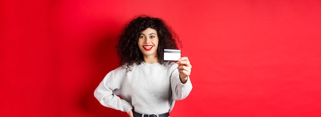 Beeld van moderne vrouw met krullend haar die hand uitstrekken en plastic creditcard tonen die bedelaars aanbevelen