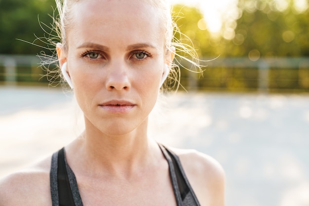 Beeldclose-up van vrouwelijke sportvrouw die trainingspak en oordoppen draagt die buiten lopen