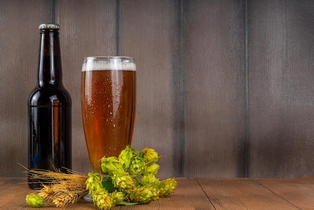 ビール瓶とホップ コーンのグラス新鮮なクラフト ビールと食材は、木製の背景にスペースをコピーします