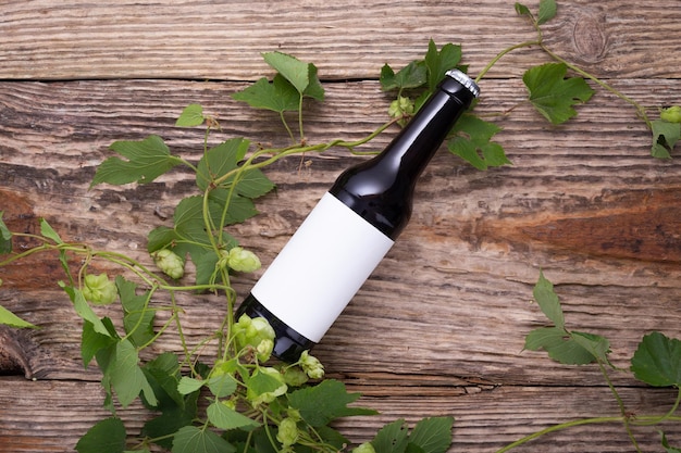 Beer bottle lies on wooden background with hop cones close up White label mock up