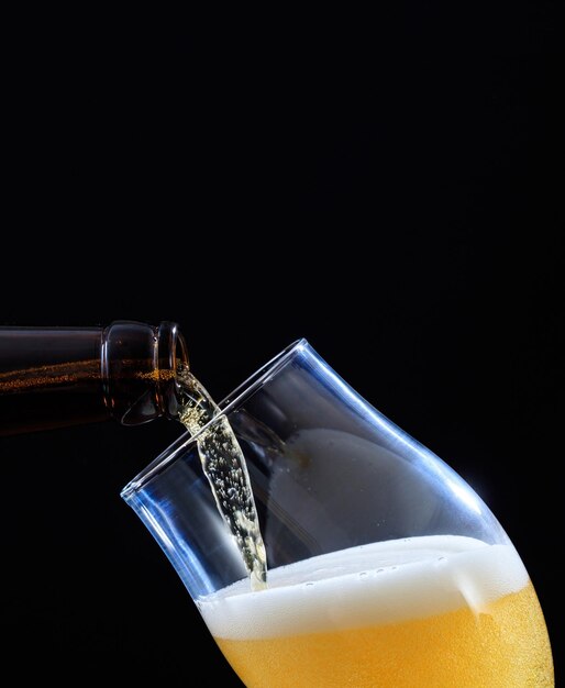 Beer bottle pouring beer in a glass black background closeup\
view