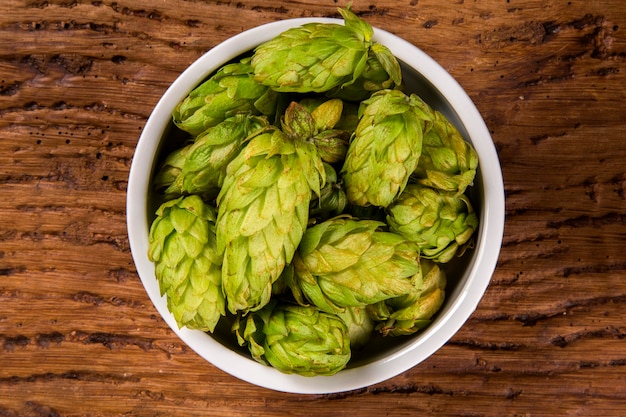 Beer brewing ingredients Hop cones in white bowl on wooden background. Beer brewery concept.