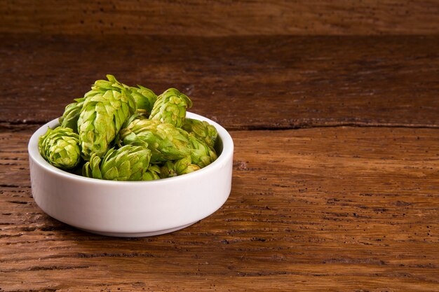 Beer brewing ingredients Hop cones in white bowl on wooden background. Beer brewery concept.