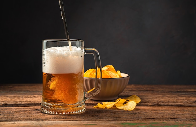 Beer and chips on a brown background. Pouring beer into a glass. Side view, space for copying.