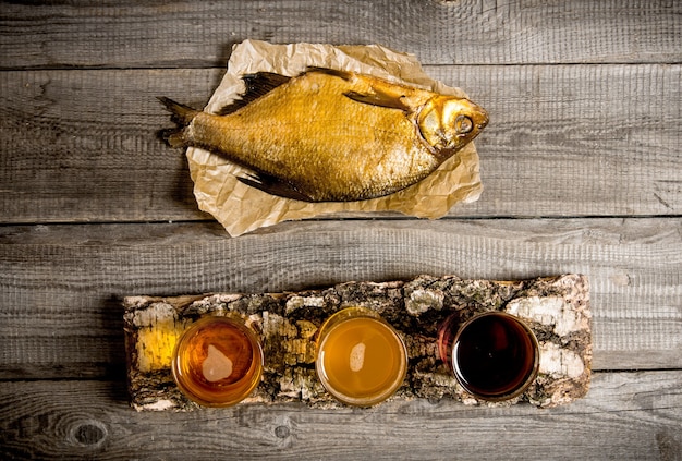 ビールのコンセプト。白樺の燻製魚と新鮮なビール3本が木製のテーブルの上に立っています。上面図