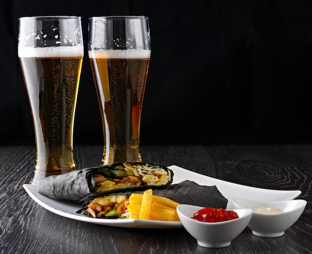 Beer in a glass and shawarma in pita bread is cut and lies on a wooden surface