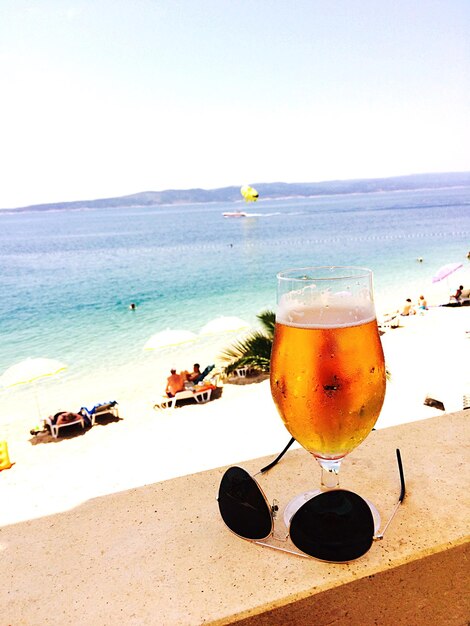 Beer glass and sunglasses on retaining wall by beach