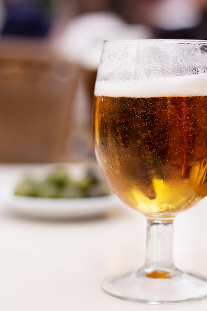 Beer in a glass on a table outdoors with olives in the background