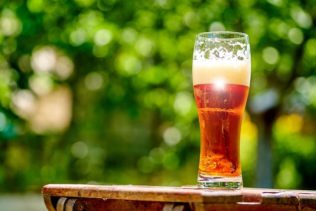 Beer in glass on wooden table with blurred city park on background natural background Closeup