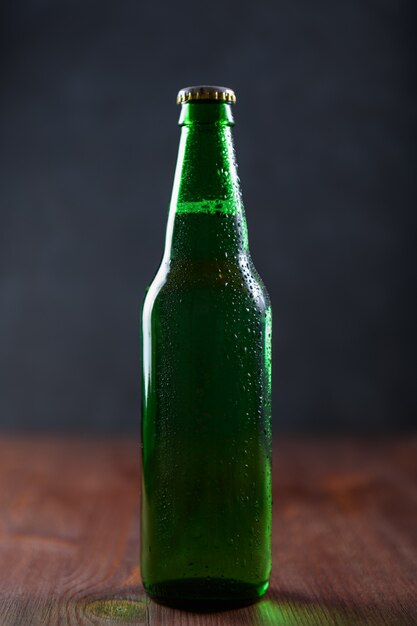 Beer in a green bottle with water drops on wooden table on dark wall