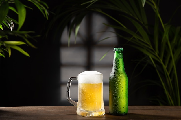 Beer mug and bottle on dark background on wooden base.