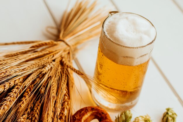 사진 맥주 잔, 홉 콘, 호밀과 밀의 이삭, 흰색 나무에 프레즐