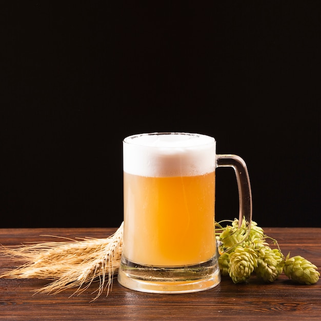 Photo beer mug with barley and hops on wooden board