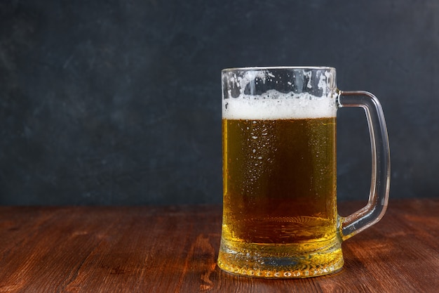 Birra in una tazza con gocce d'acqua sul tavolo di legno su backgroun scuro