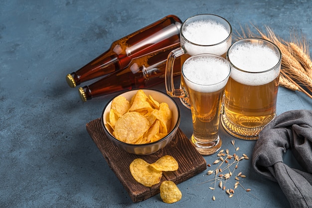 Beer mugs and bottles chips and wheat on a dark background Horizontal view space for copying