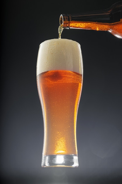 Beer pouring in cup from the bottle against black background