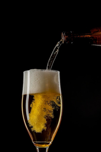 A beer pouring in a glass on a black background.