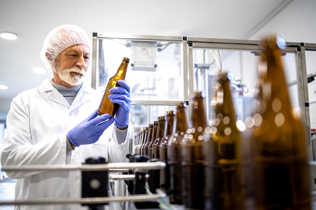 Beer production factory and experienced worker checking glass bottles before filling