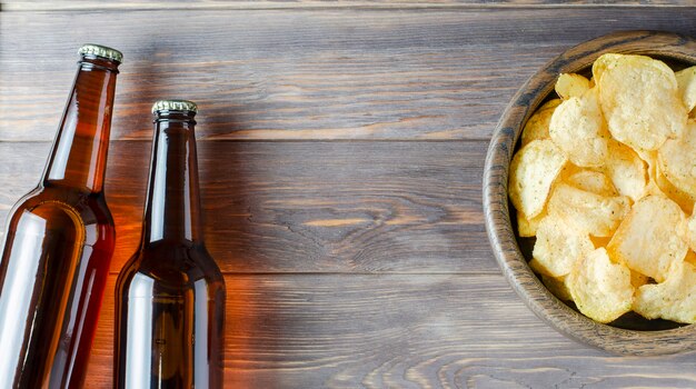 Beer and salted potato chips on a plate on a brown wooden