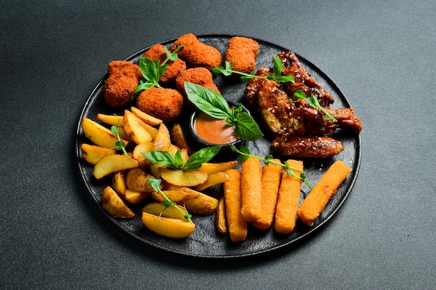 Beer snack plate chicken nuggets chicken wings cheese and fries On a dark background closeup