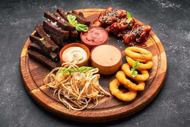 Beer snack on a wooden board onion rings croutons squid grilled chicken wings and sauces