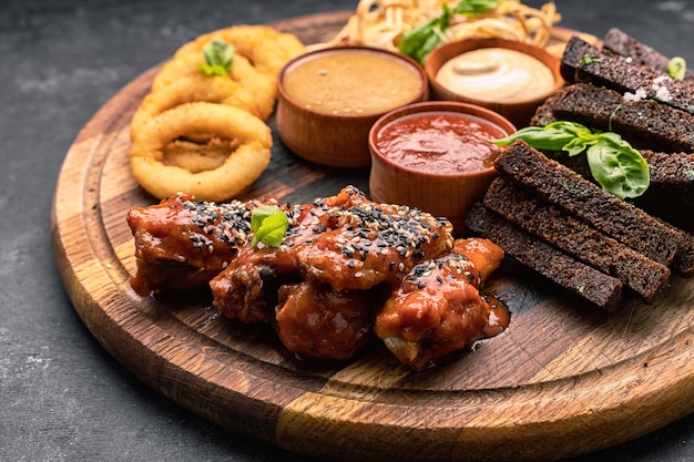 Beer snack on a wooden board onion rings croutons squid grilled chicken wings and sauces