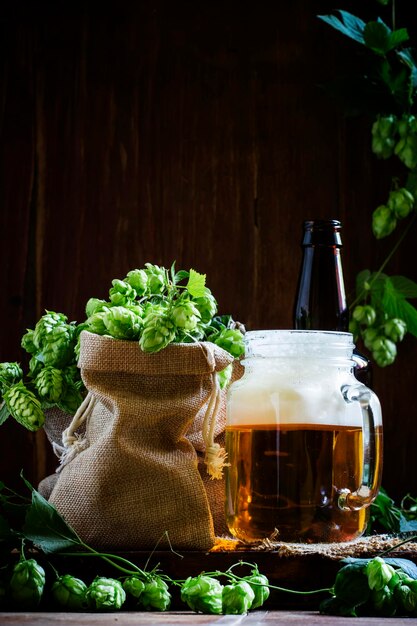 ガラス瓶の茶色のボトルに泡とヴィンテージの木製の背景の素朴なスタイルの新鮮な緑のホップのコーンとビールローキーセレクティブフォーカス