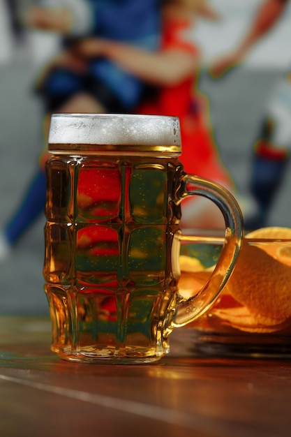 Пиво с закусками на деревянном столе на фоне футбольного поля, концепция спорта и развлечений вертикальное изображение