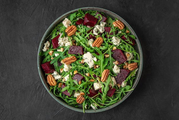 Beet or beetroot salad with fresh arugula, blue cheese and pecan nuts in a plate on black surface