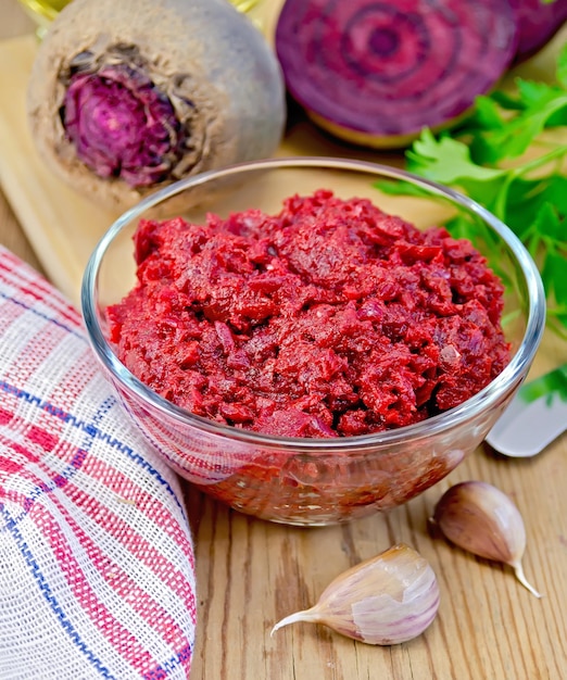 Beet caviar in the glass bowl, garlic, beets, parsley, napkin on the background of wooden boards