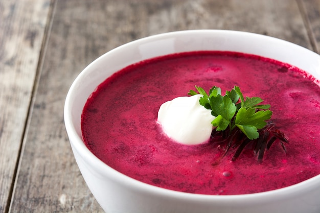 Beet soup in white bowl on wooden table close up