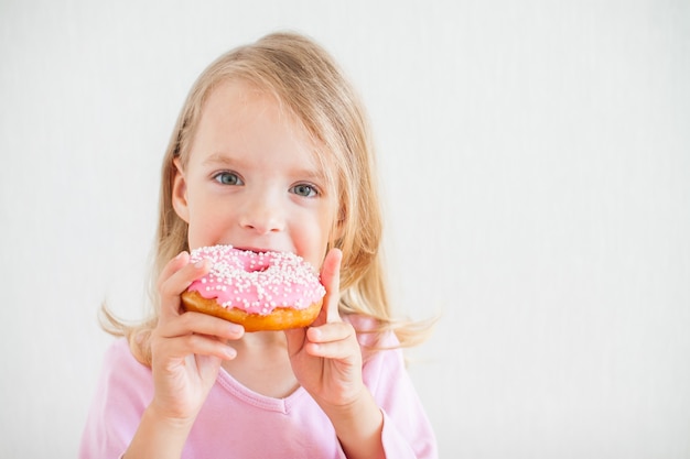 Beetje blij meisje met blond haar spelen en donuts met roze suikerglazuur proeven bij de viering van de chanoeka