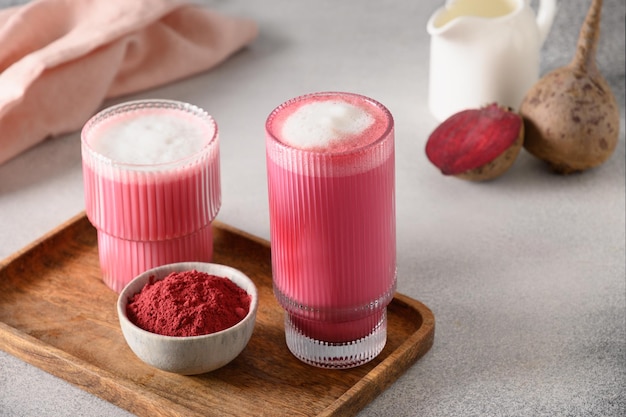 회색 배경에 있는 유리 컵에 있는 비트루트 라떼 또는 핑크 문 우유 라떼 훌륭한 온난화 음료