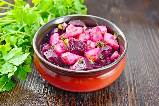 Beetroot and potato salad seasoned with vegetable oil and vinegar in a bowl parsley against a dark wooden board