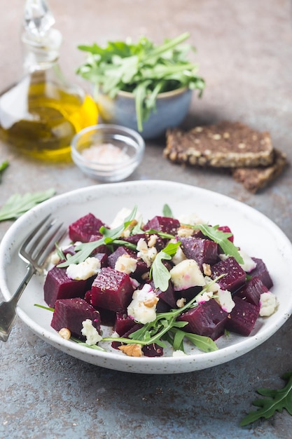 Insalata di barbabietole con formaggio blu, rucola e noci in un piatto bianco su sfondo grigio