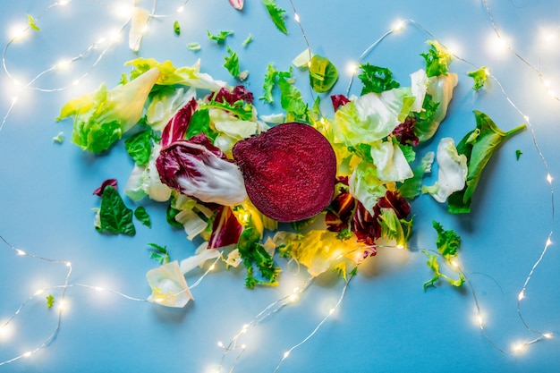 Beetroot and salad with fairy lights on blue surface. Above view