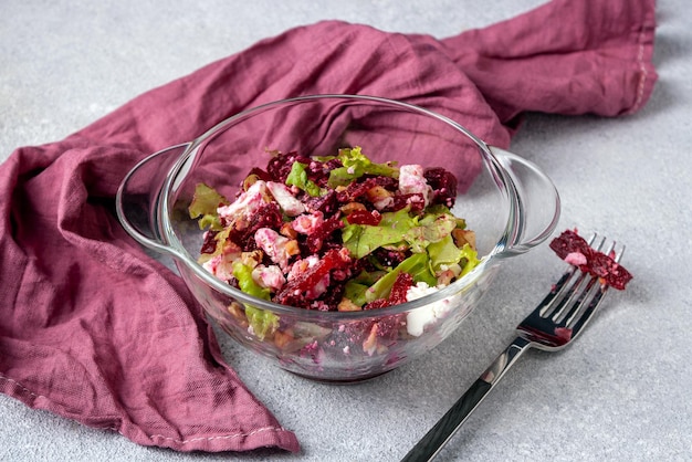 Beetroot and soft cheese salad in a glass bowl red napkin fork on a gray background