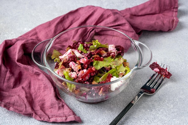 Insalata di barbabietole e formaggio morbido in una ciotola di vetro forchetta tovagliolo rosso su sfondo grigio