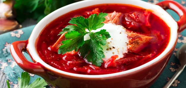 Beetroot soup with meat, sour cream and parsley in a brown ceramic bowl on the old wooden background. Borsch- traditional dish of Ukrainian cuisine. Selective focus.