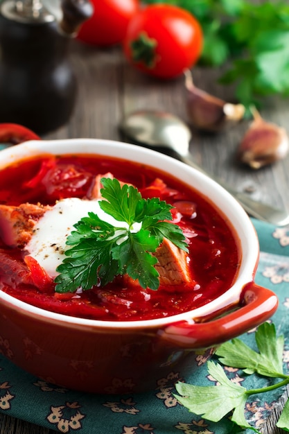 Beetroot soup with meat, sour cream and parsley in brown ceramic bowl