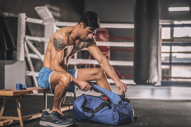 Before workout. Muscular build man sitting in a changing room in a gym