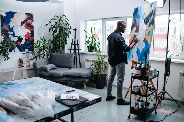 Begaafde zwarte man schildert op een ezel in zijn atelier in appartement
