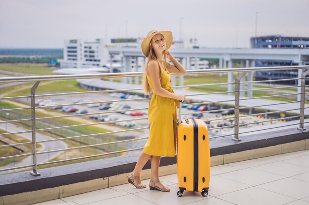 Begin van haar reis Mooie jonge vrouw lreiziger in een gele jurk en een gele koffer wacht op haar vlucht