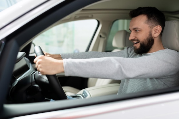 Beginnende bestuurder achter het stuur van een nieuwe auto kijkt met een glimlach vooruit