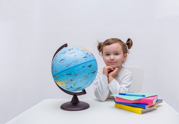 The beginning of the school year. small, beautiful pupil sits at a table and looks at the camera on a white isolated